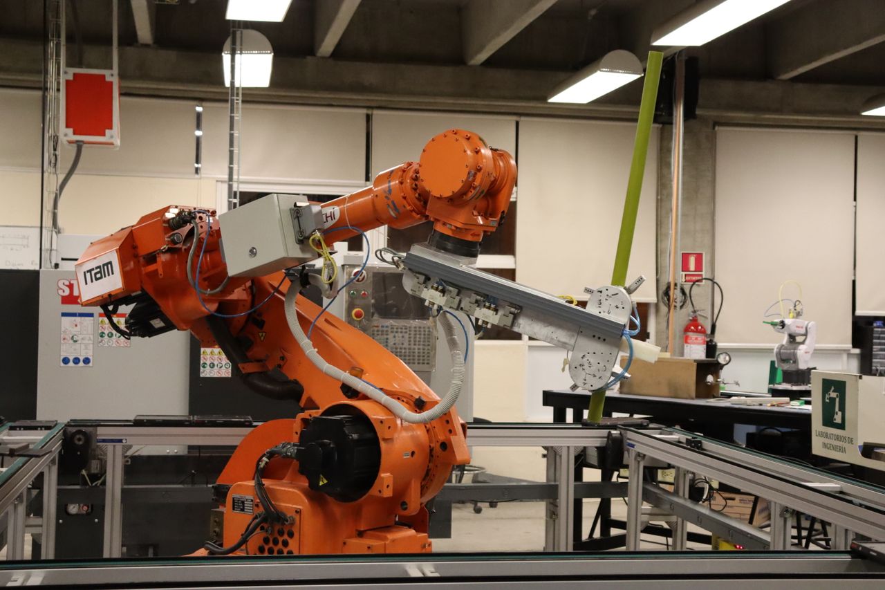 An orange industrial robot arm beside a conveyor rig in an engineering laboratory.